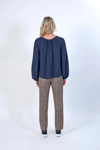 Woman wearing navy blouse and beige plaid check trousers, shown from the back, studio setting
