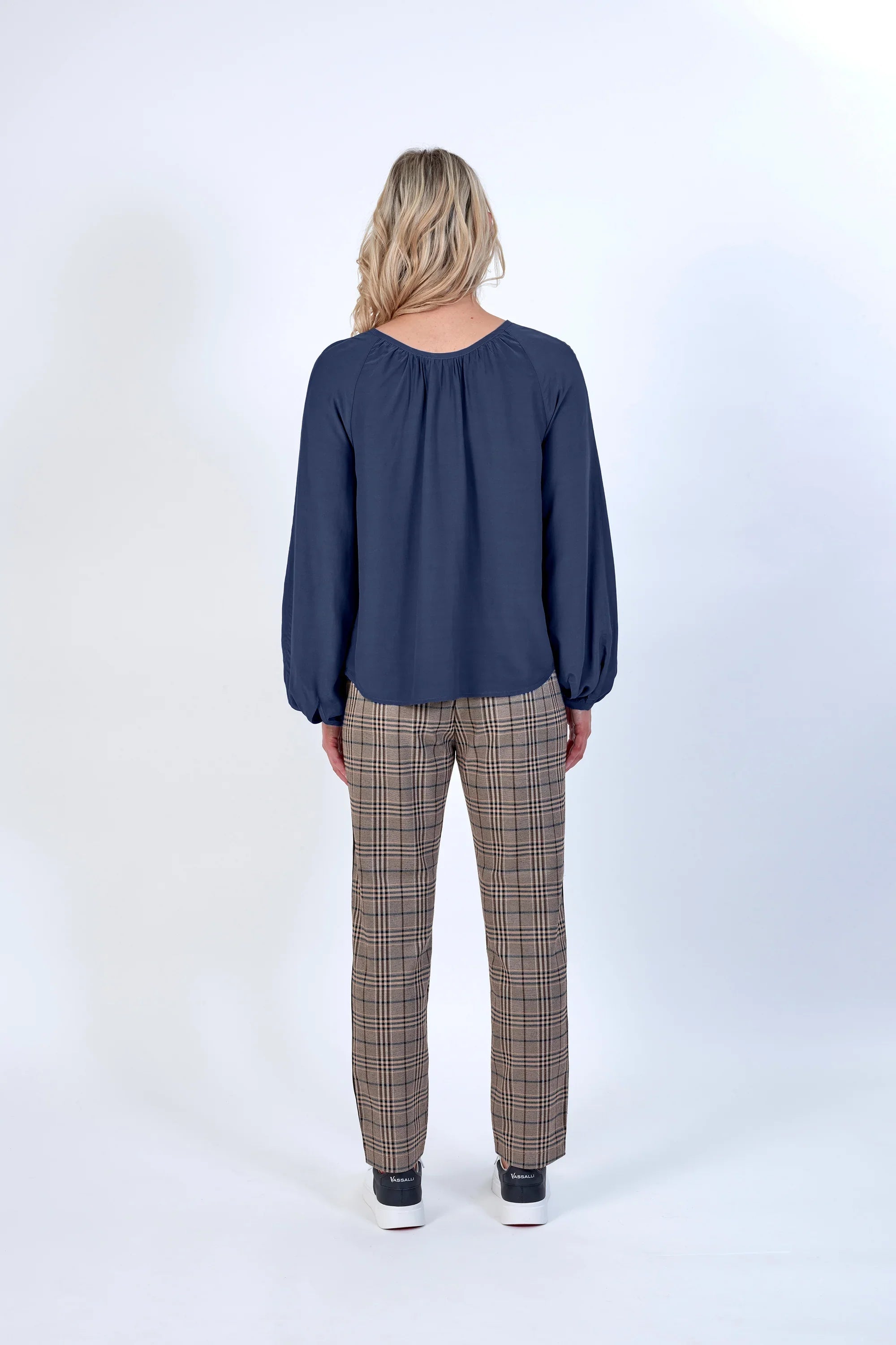 Woman wearing navy blouse and beige plaid check trousers, shown from the back, studio setting