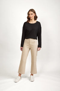 Woman wearing beige wide leg jeans, black long sleeve top, and white sneakers on white background