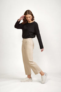 Woman wearing oat-colored wide leg denim jeans, black long sleeve top, and white sneakers