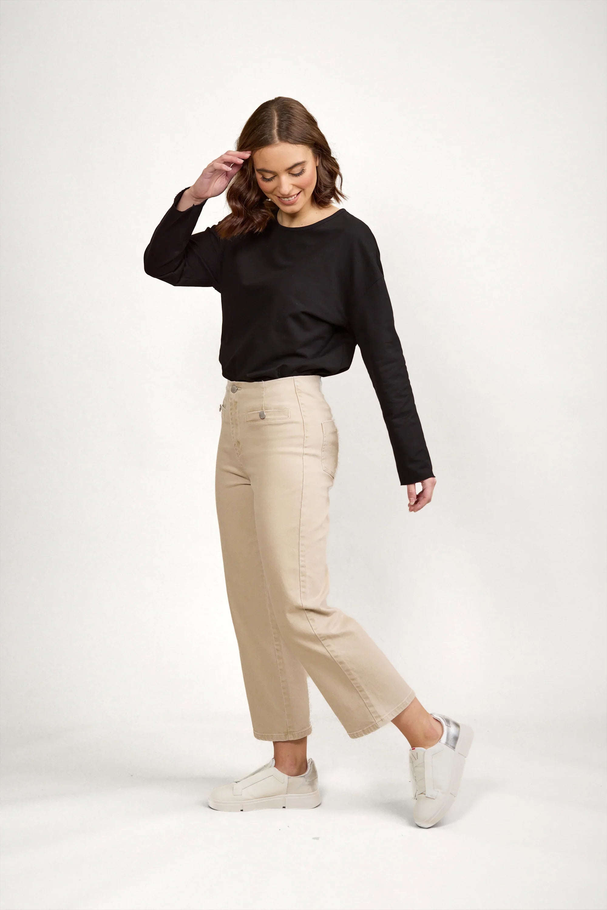 Woman wearing oat-colored wide leg denim jeans, black long sleeve top, and white sneakers