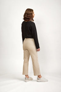 Woman wearing oat-colored denim jeans with straight leg, black long sleeve top, and white sneakers, standing against a neutral background