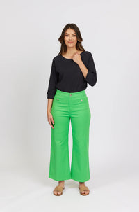 Woman in black long sleeve top and bright green wide-leg jeans with sandals, studio background