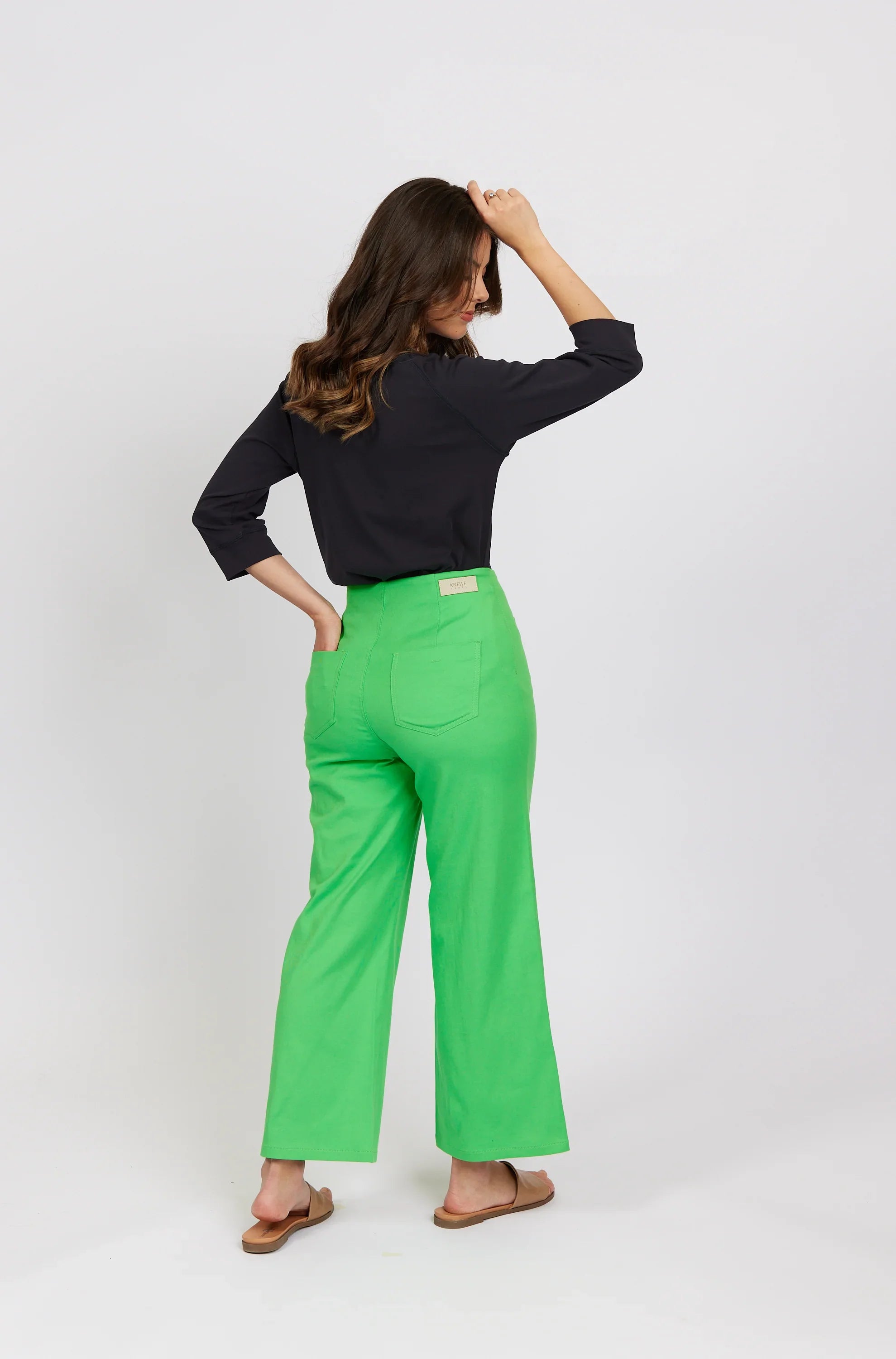 Woman wearing bright green wide-leg jeans and a black top, standing against a plain background