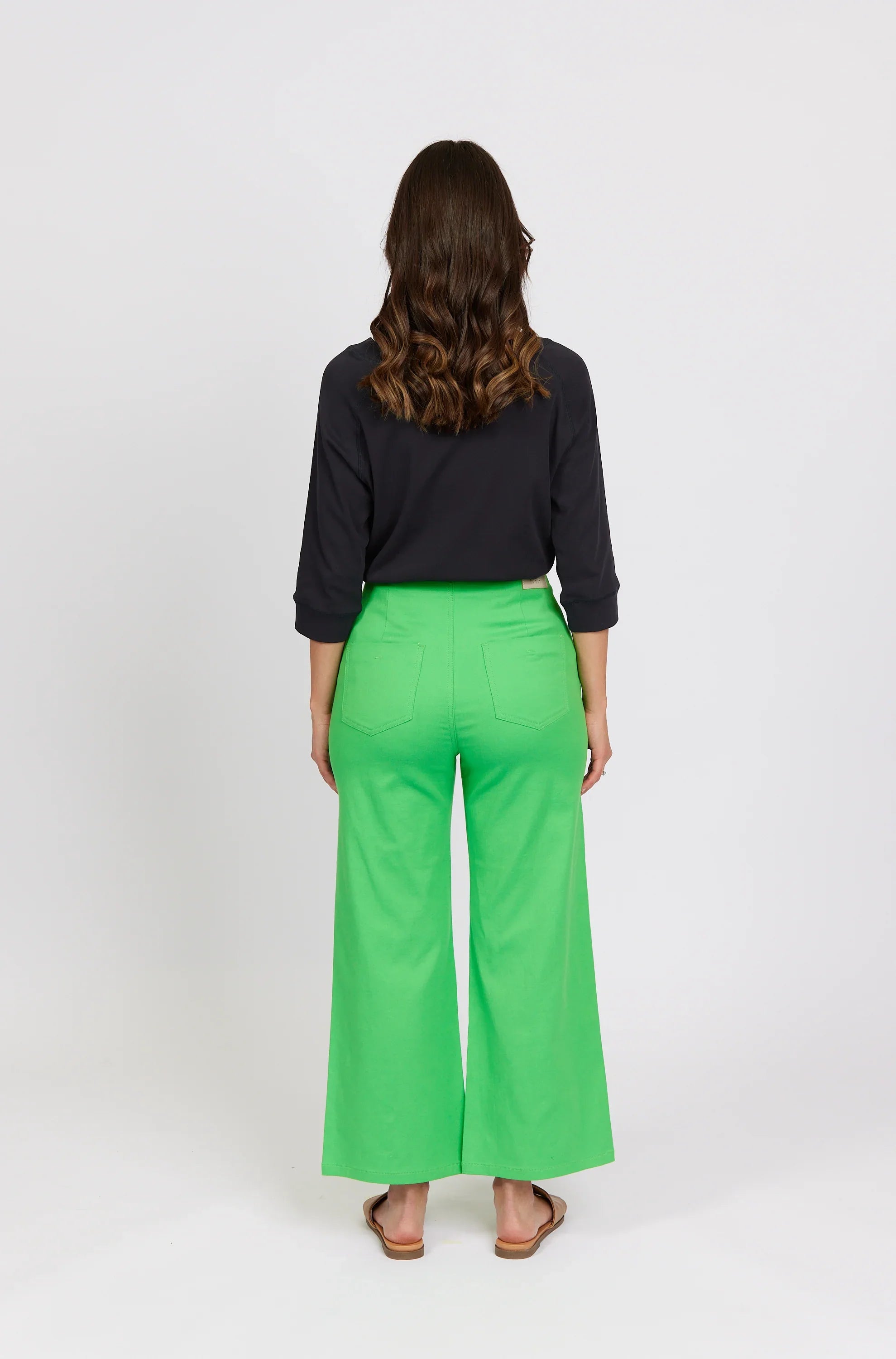 Woman in black blouse and bright green wide-leg pants, standing in studio, back view