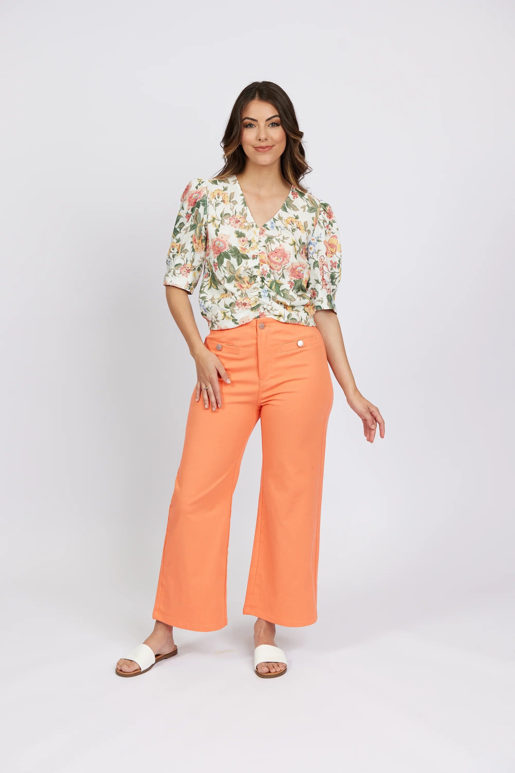 Woman wearing apricot wide-leg jeans, floral blouse, and white sandals on white background