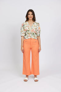 Woman wearing apricot wide-leg jeans, floral blouse, and white sandals, front view