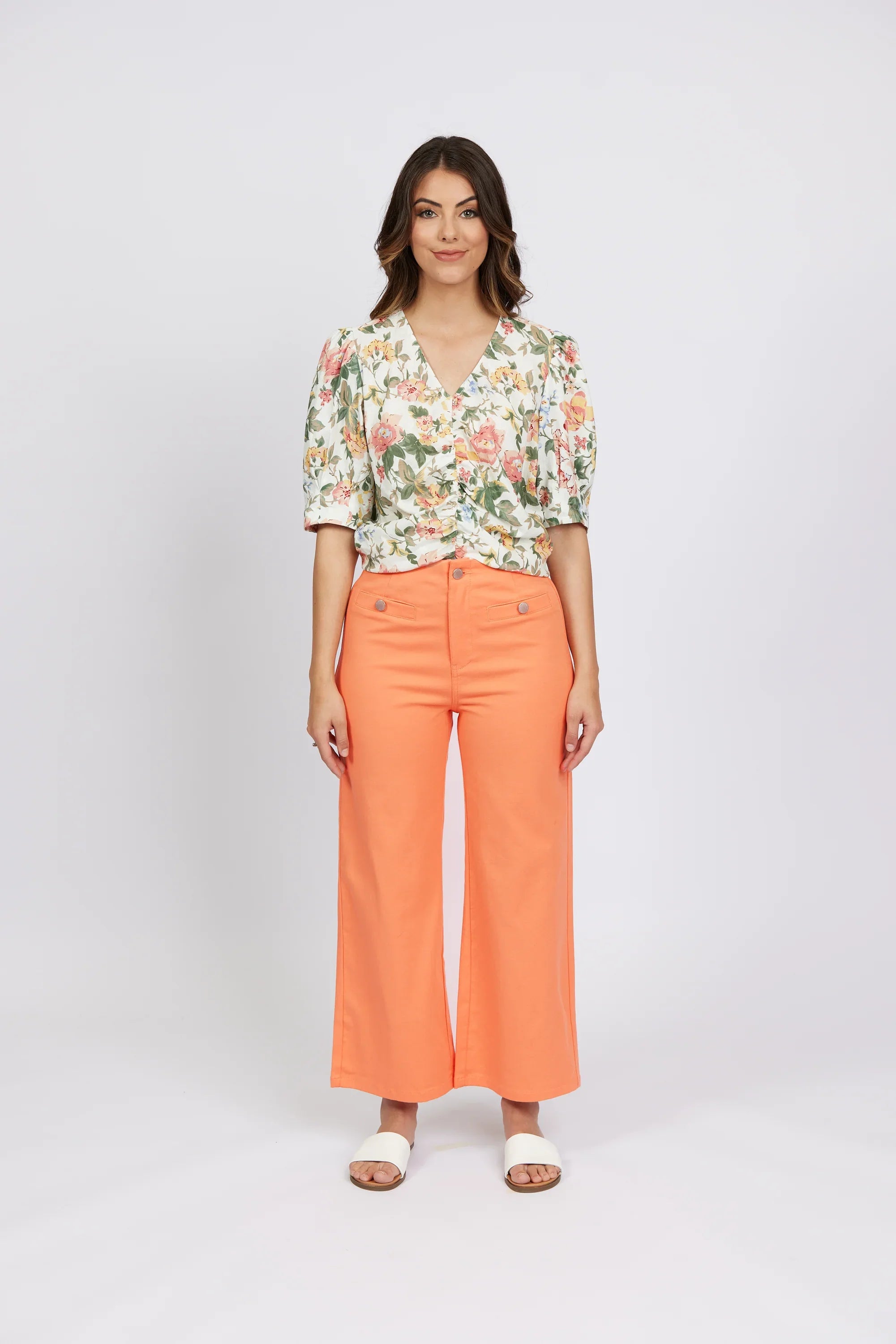 Woman wearing apricot wide-leg jeans, floral blouse, and white sandals, front view