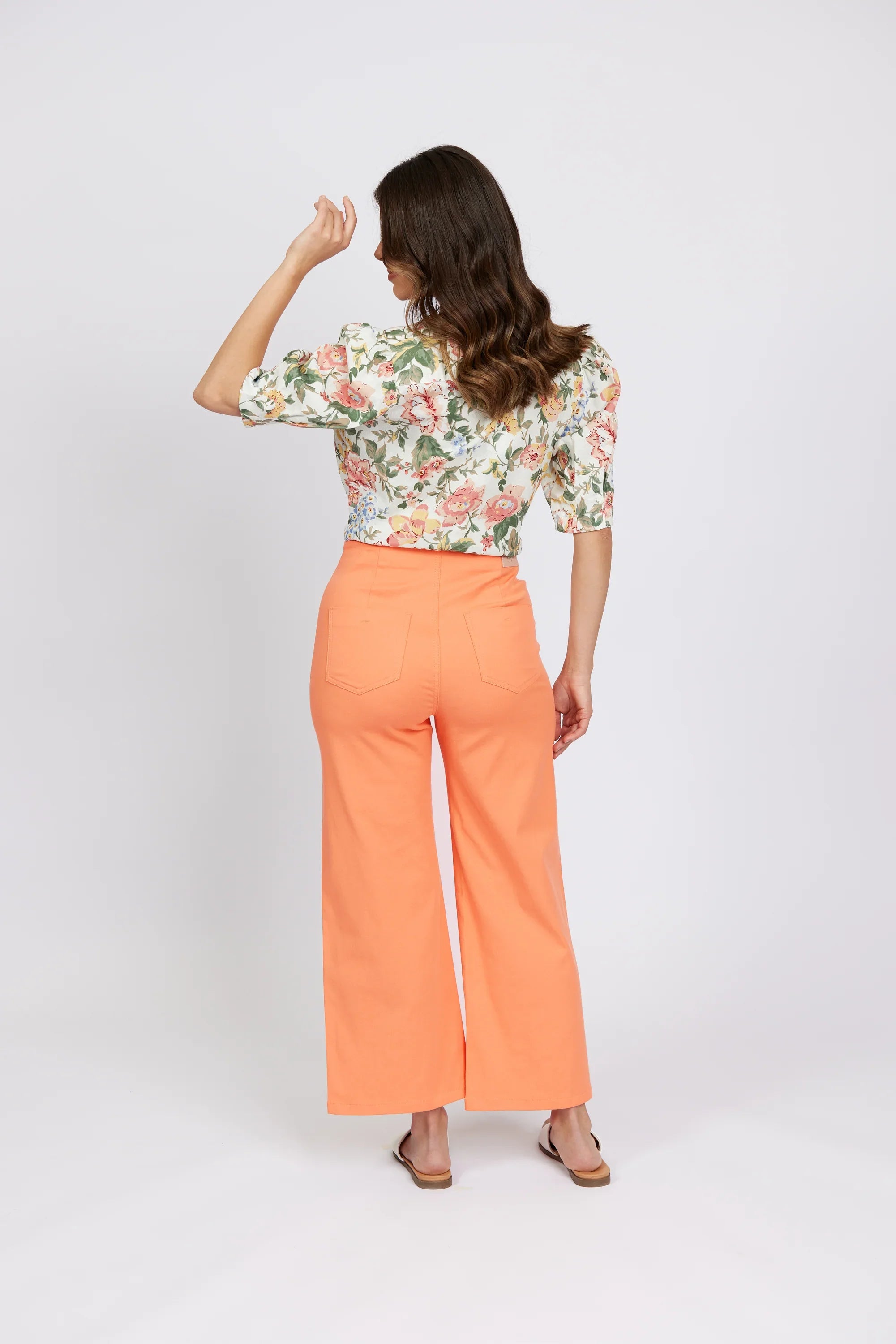 Woman wearing high-waisted apricot wide-leg jeans and floral blouse, back view