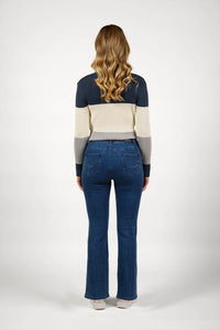Woman in blue wash flared jeans and a color block sweater, standing facing backward