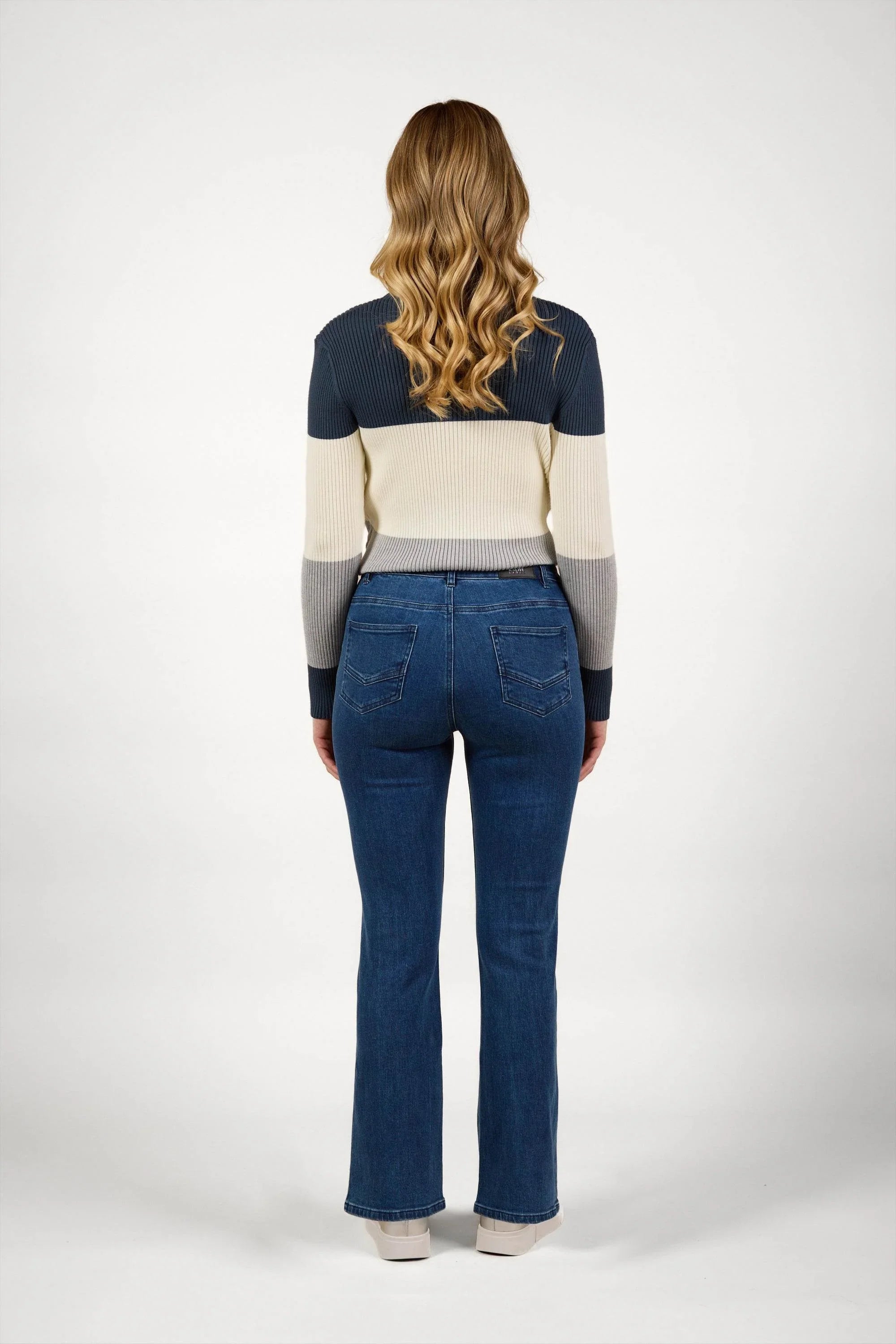 Woman in blue wash flared jeans and a color block sweater, standing facing backward