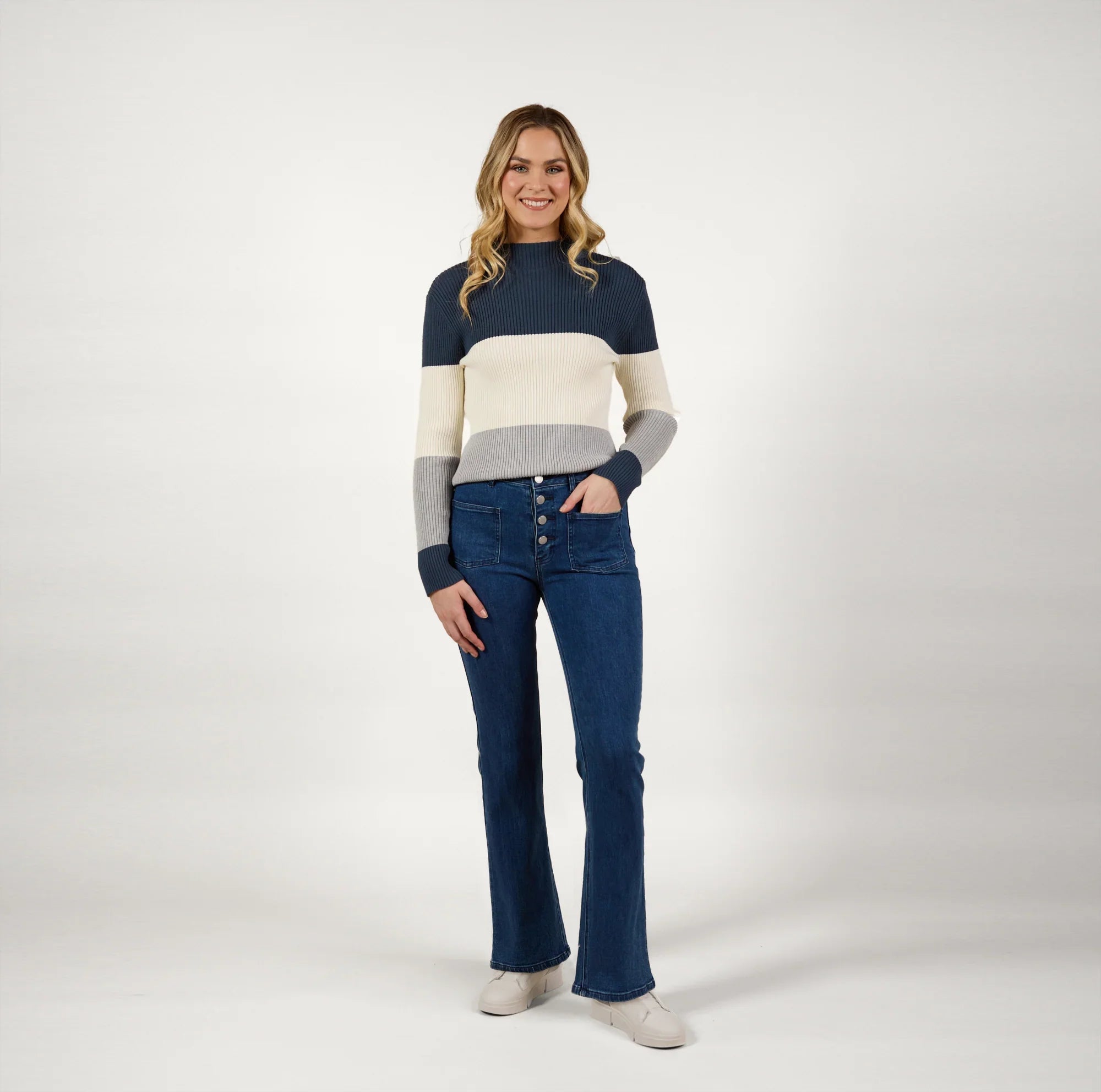 Woman wearing blue wash flared jeans and striped knit sweater, standing in studio