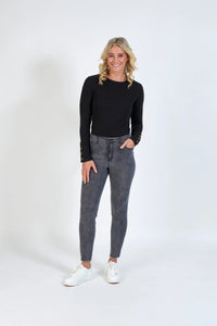 Woman wearing grey skinny jeans, black long sleeve top, and white sneakers, posing against a plain white background.