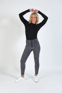 Woman wearing grey skinny jeans and black long-sleeve top, standing on white background