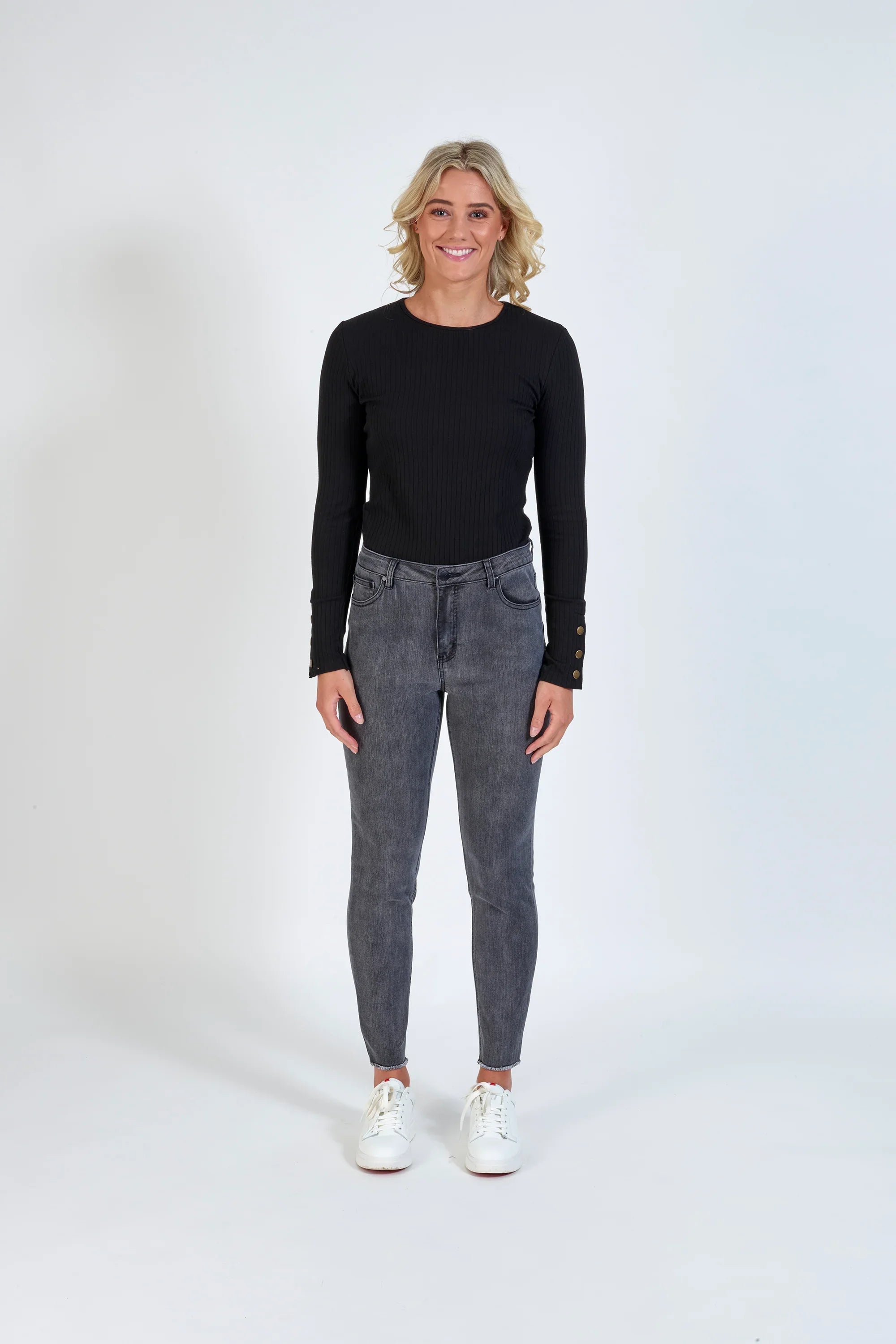 Woman wearing space grey skinny jeans, black long sleeve top, and white sneakers