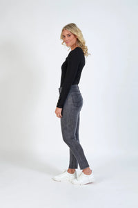 Woman in grey high-waisted skinny jeans, black ribbed top, and white sneakers on white background