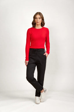 Woman in black drawstring pants with white side stripes, red ribbed top, and white sneakers