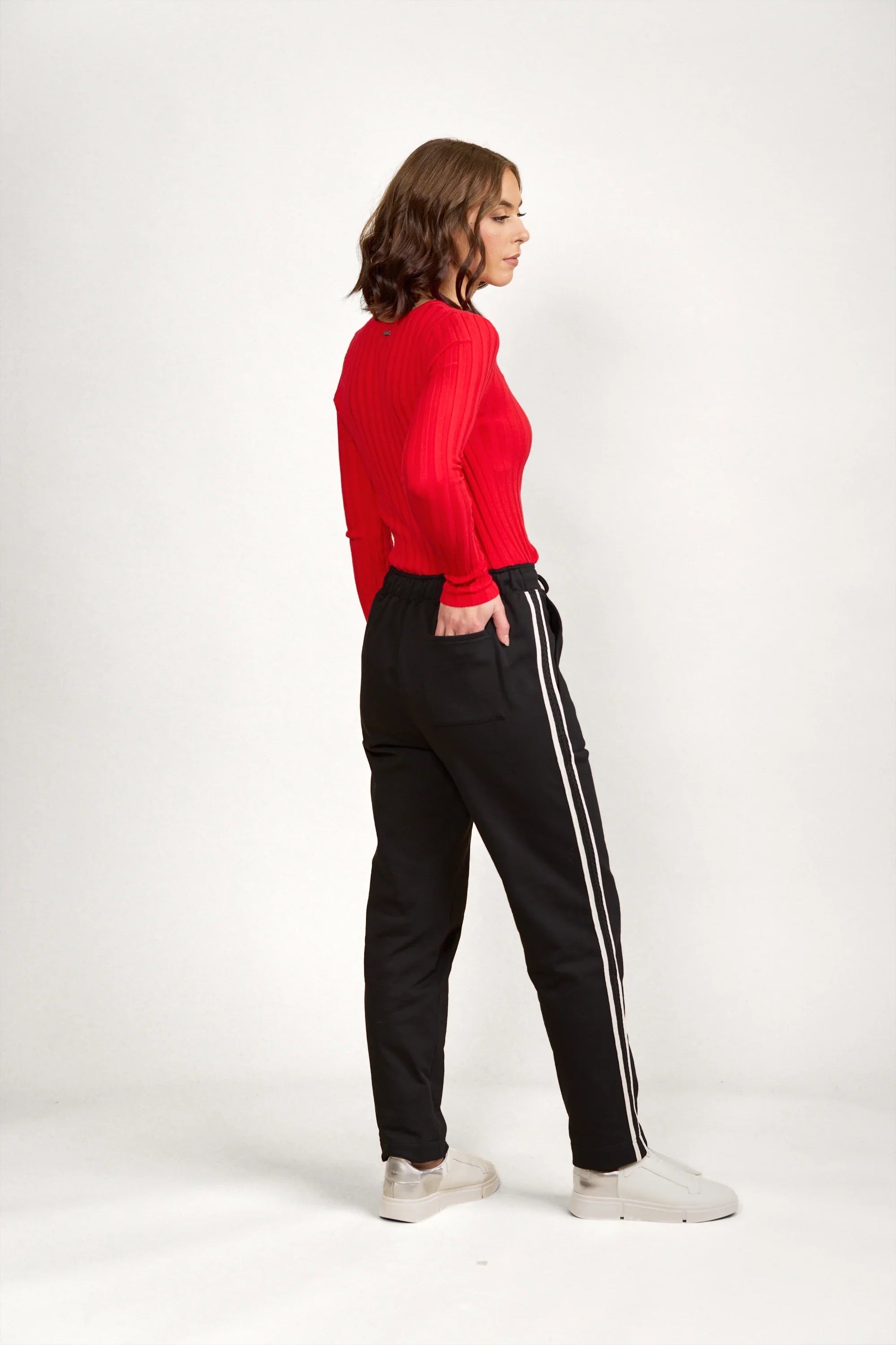 Woman wearing black pants with white side stripes, red ribbed long sleeve top, and white sneakers