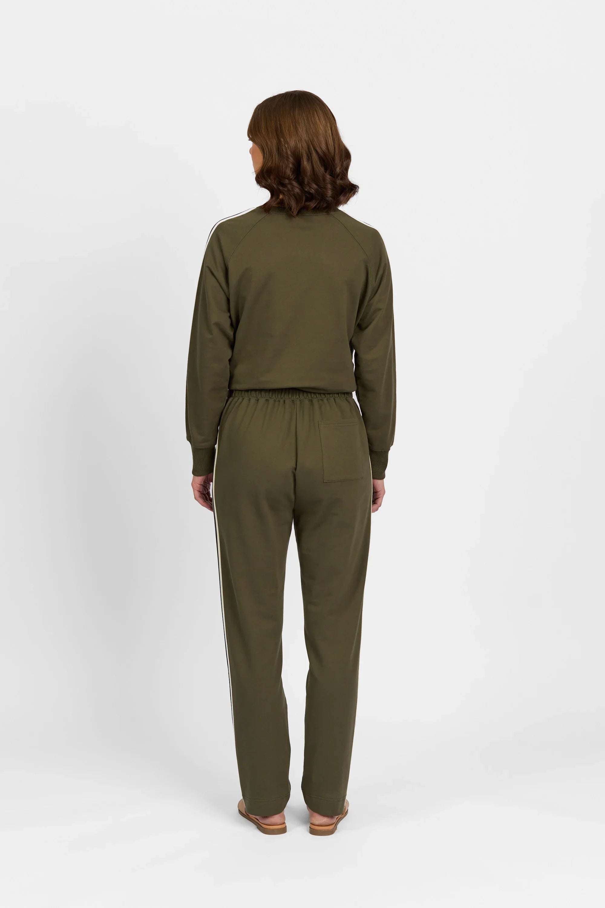 Back view of woman wearing khaki casual pants and matching long-sleeve top, white background