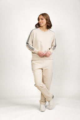 Woman wearing beige track pants and matching sweatshirt with side stripe detail, white sneakers