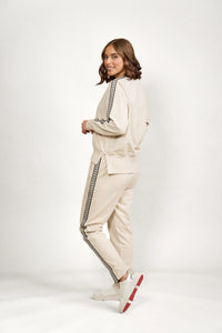 Woman wearing beige track pants and matching top with black side detailing on white background