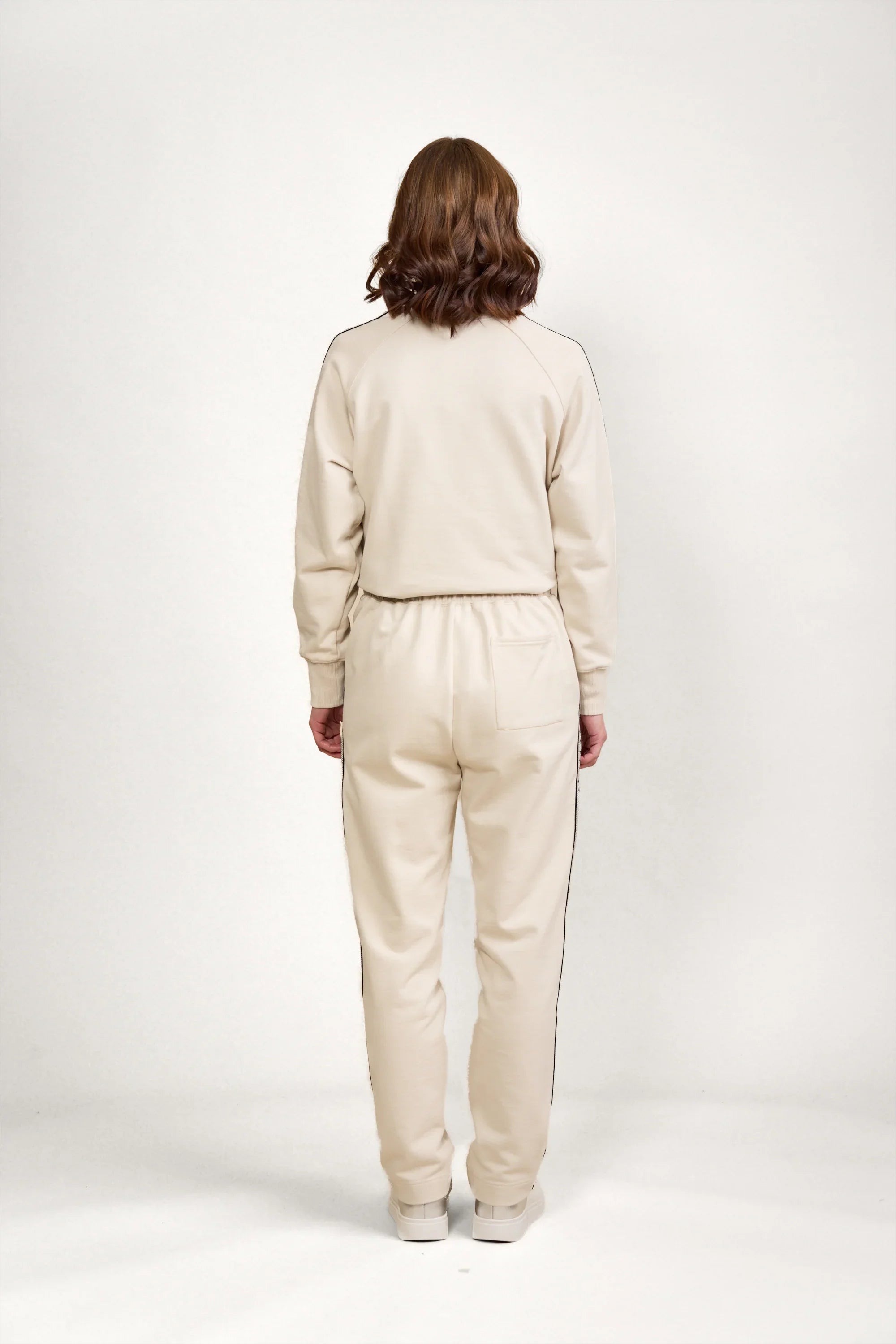 Back view of woman wearing stone-colored jogger pants and sweatshirt with black side piping