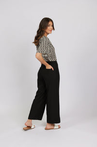 Woman models black wide-leg pants with side pockets and patterned short-sleeve top