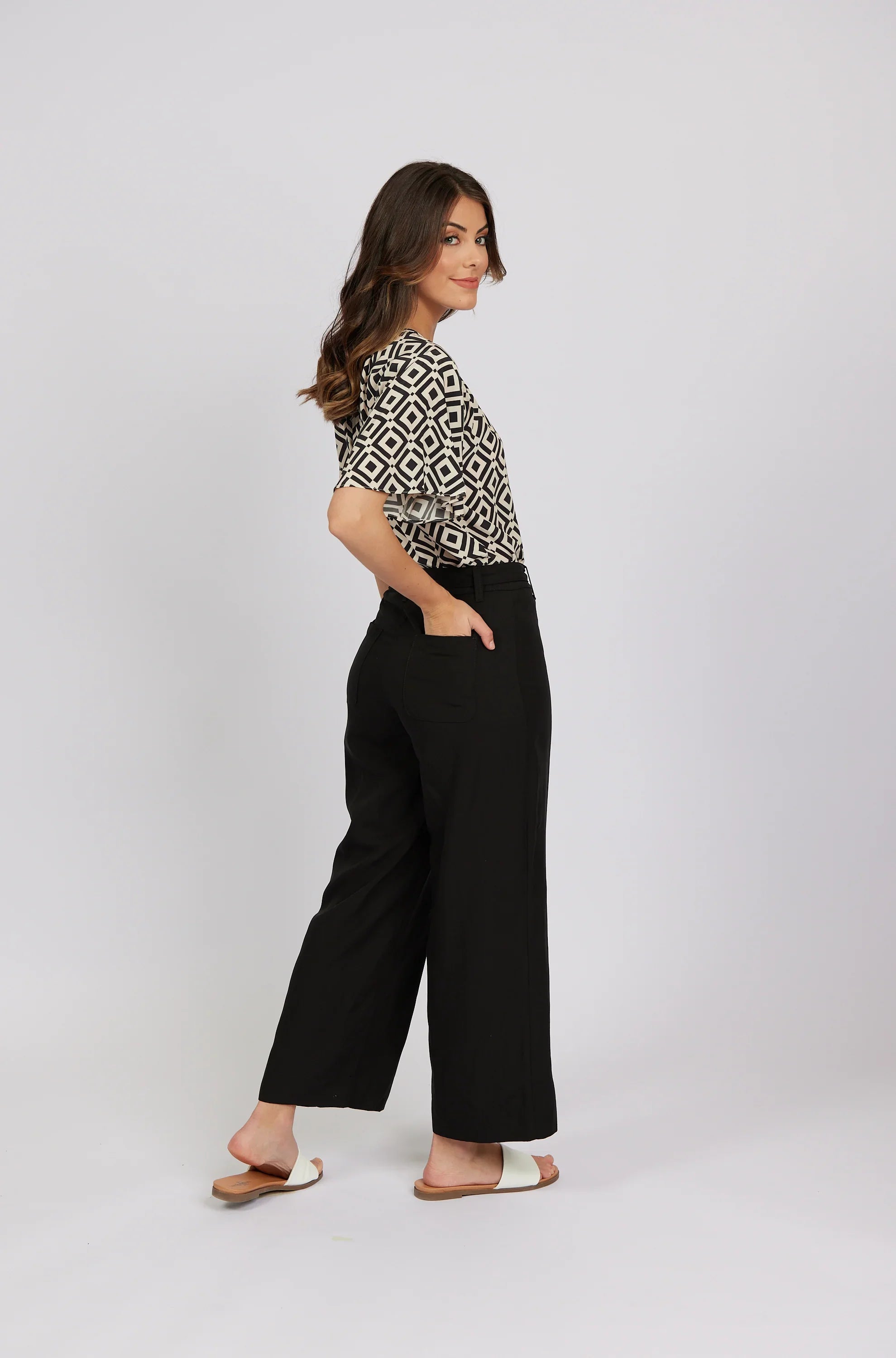 Woman models black wide-leg pants with side pockets and patterned short-sleeve top