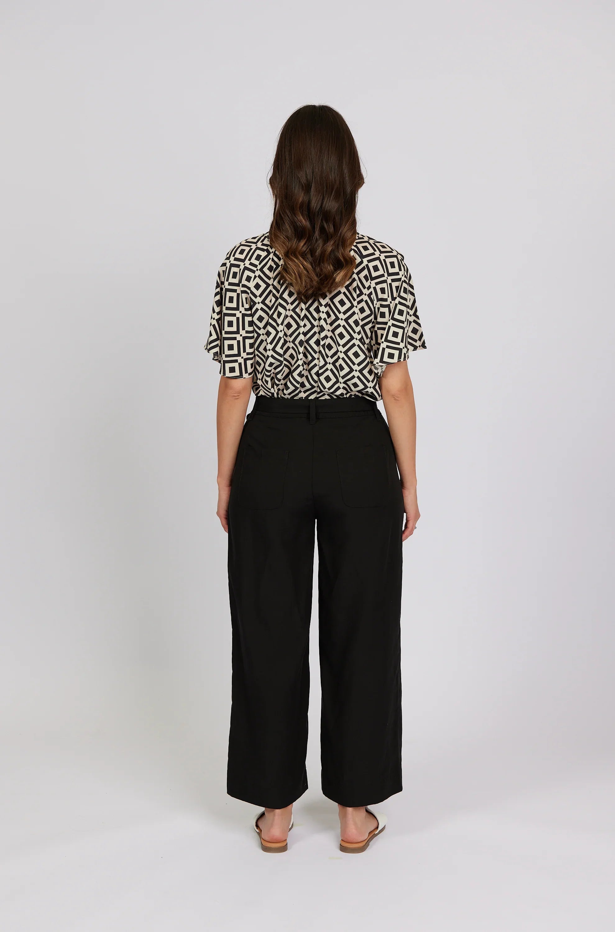 Woman wearing high-waisted black wide-leg pants and geometric print blouse, back view
