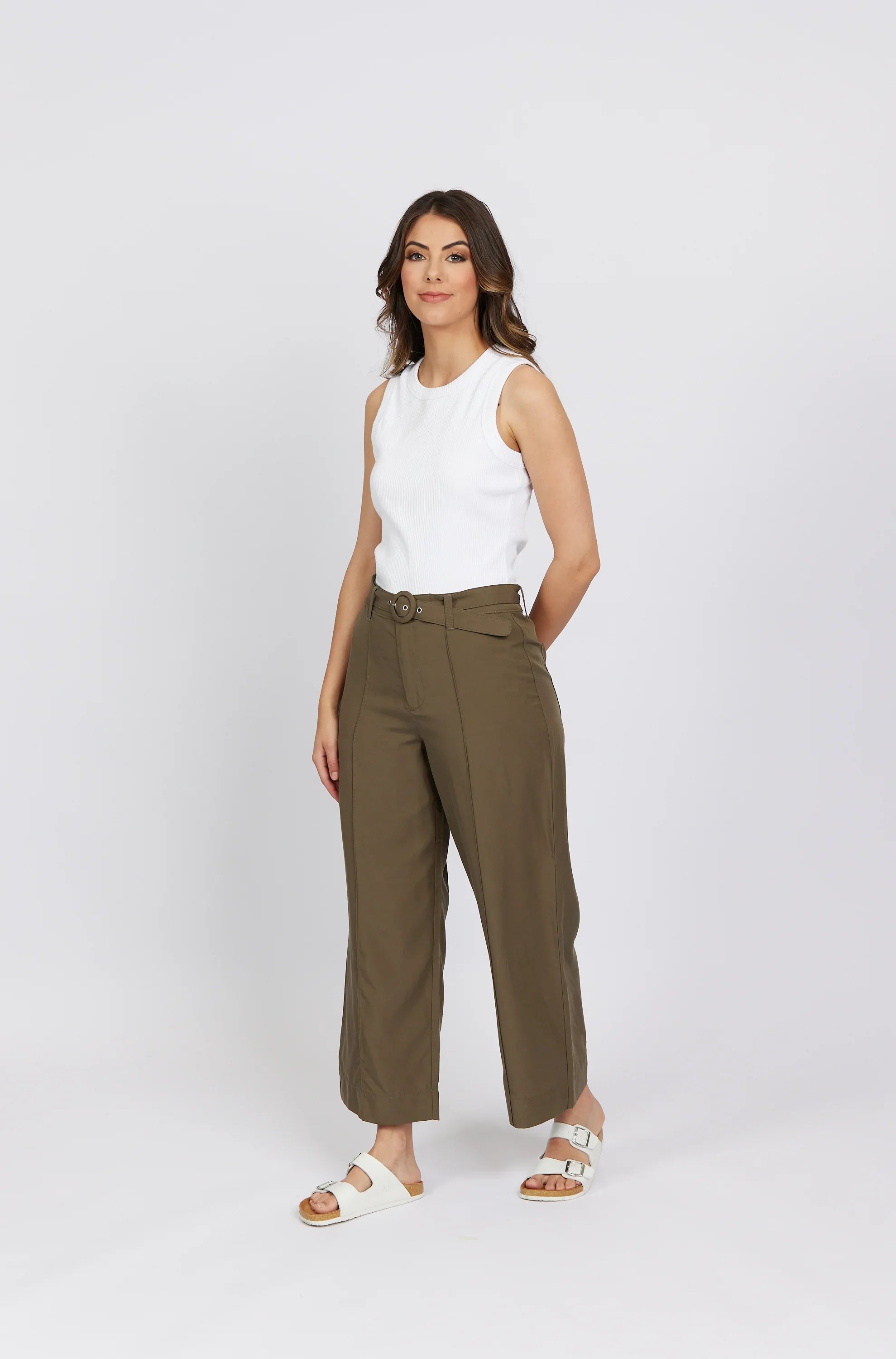 Woman in khaki wide-leg pants with belt and white sleeveless top on plain background