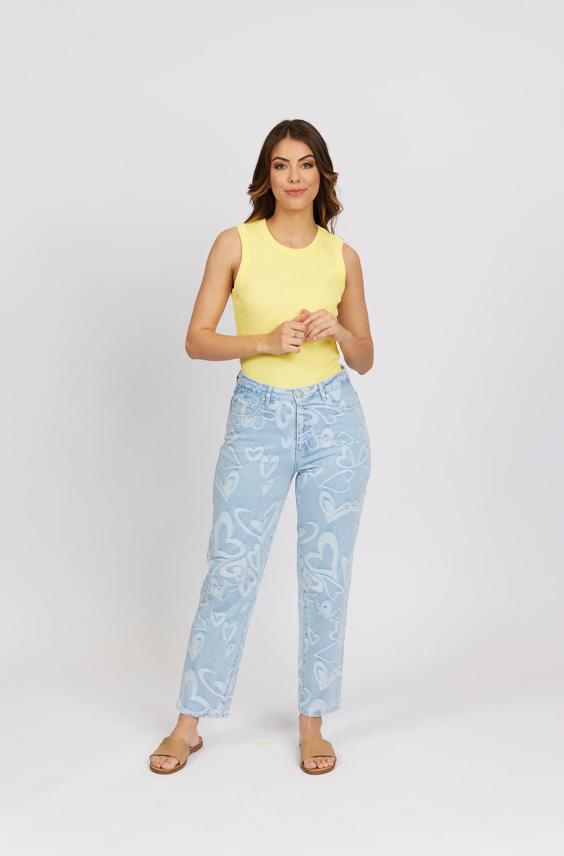 Woman wearing light blue heart print jeans, yellow sleeveless top, and tan sandals