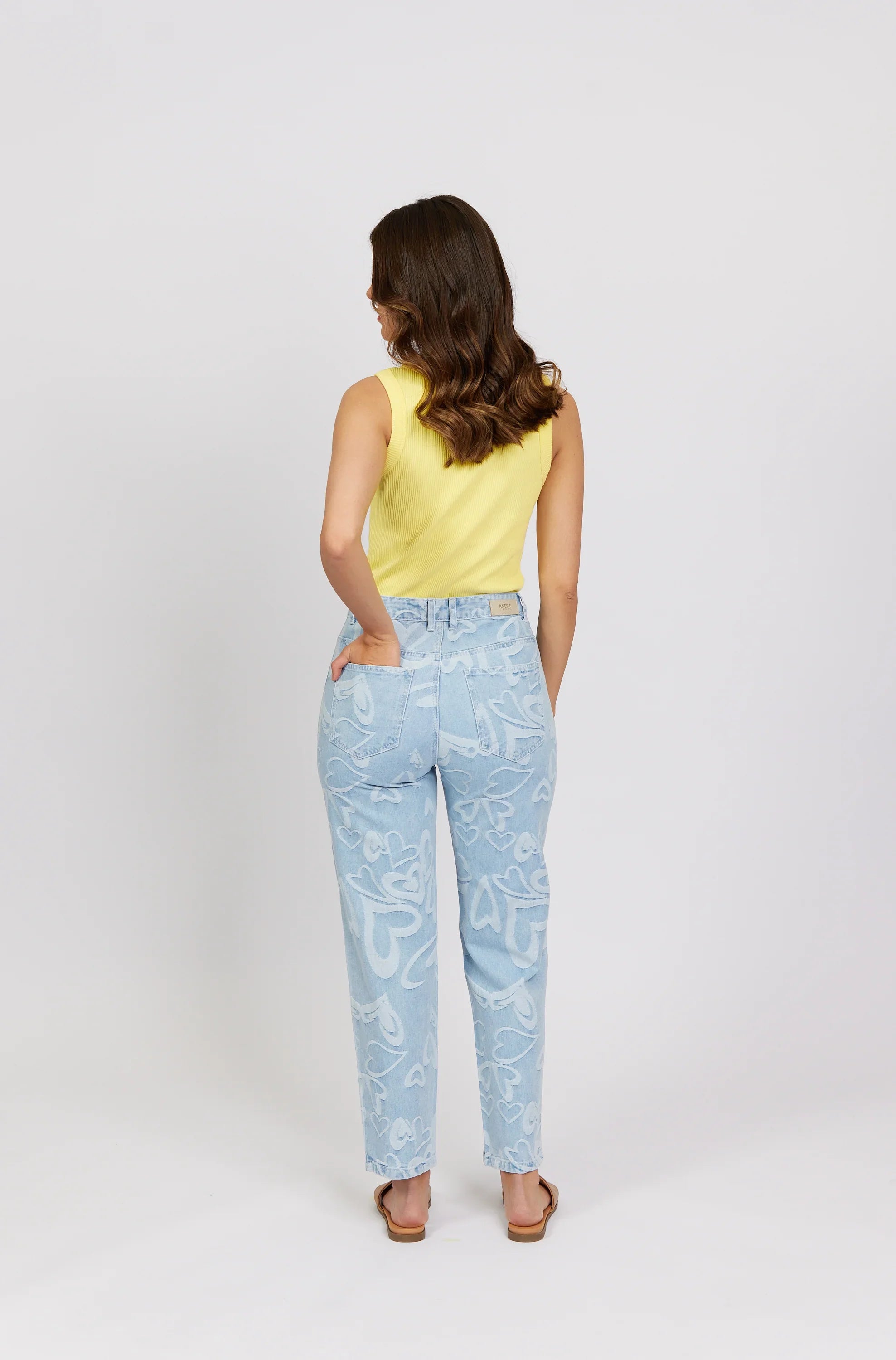 Woman in yellow tank top and light blue jeans with white heart print, back view