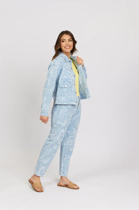 Woman wearing light blue heart-print denim jacket and jeans with tan sandals, studio background