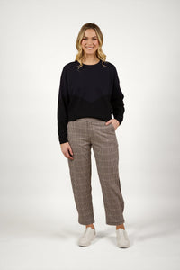 Woman wearing checked straight-leg pants, black sweater, and white sneakers standing indoors
