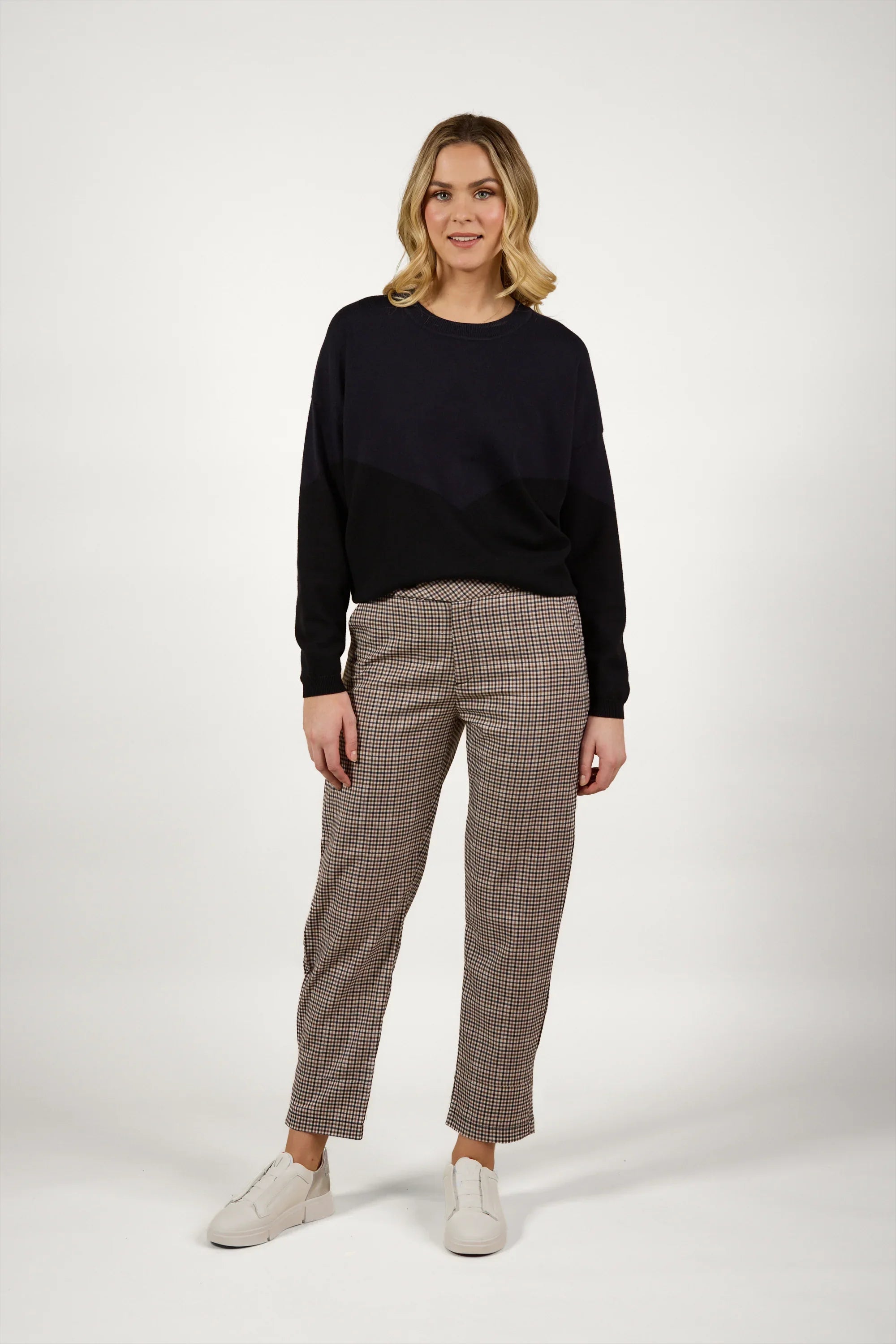 Woman wearing checked tailored pants, black sweater, and white sneakers in studio