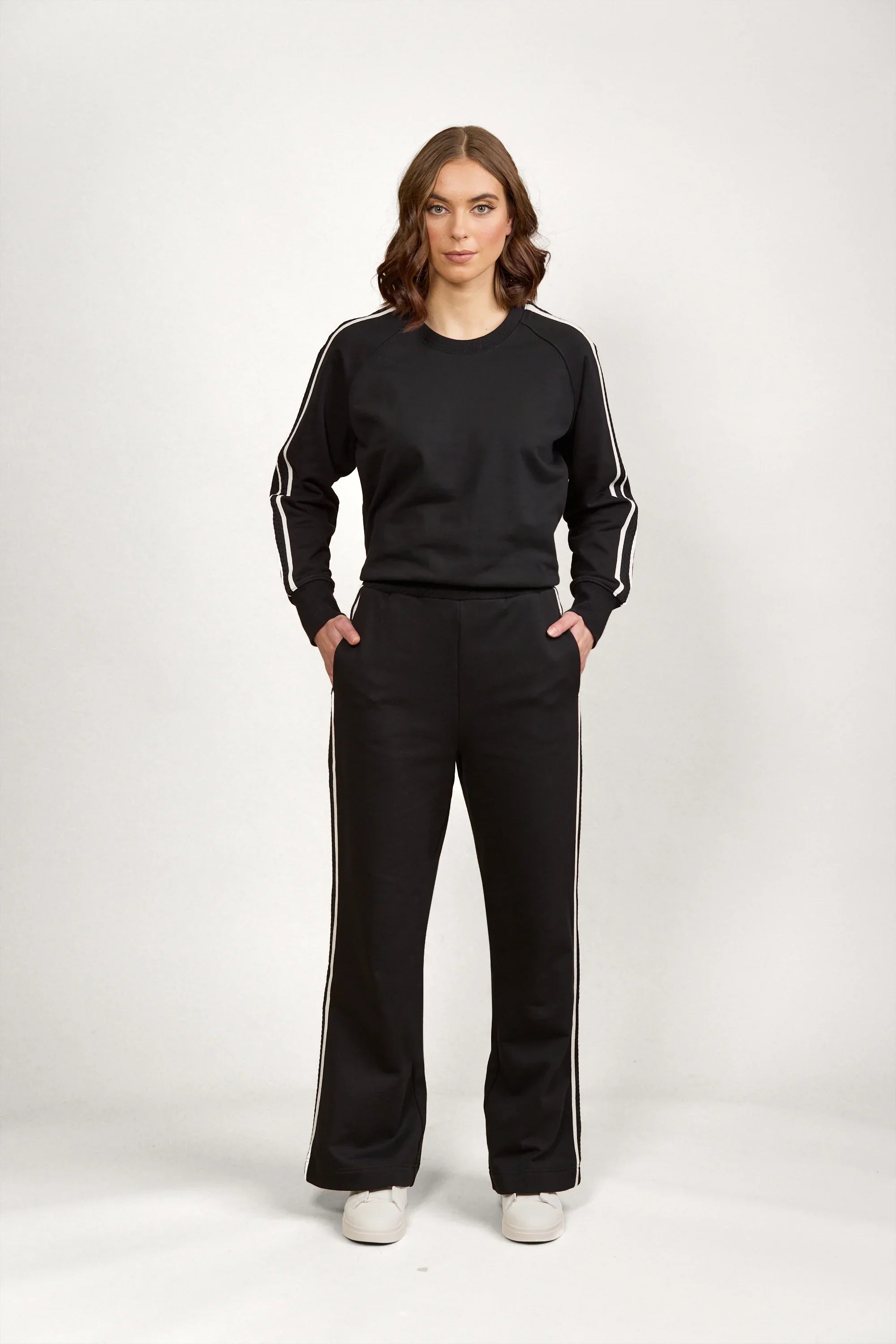 Woman wearing black wide leg pants and matching black sweatshirt with white side stripes