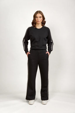 Woman wearing black wide leg pants and matching black sweatshirt with white side stripes