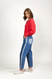 Woman in relaxed blue denim jeans with side stripe, red textured top, and white sneakers
