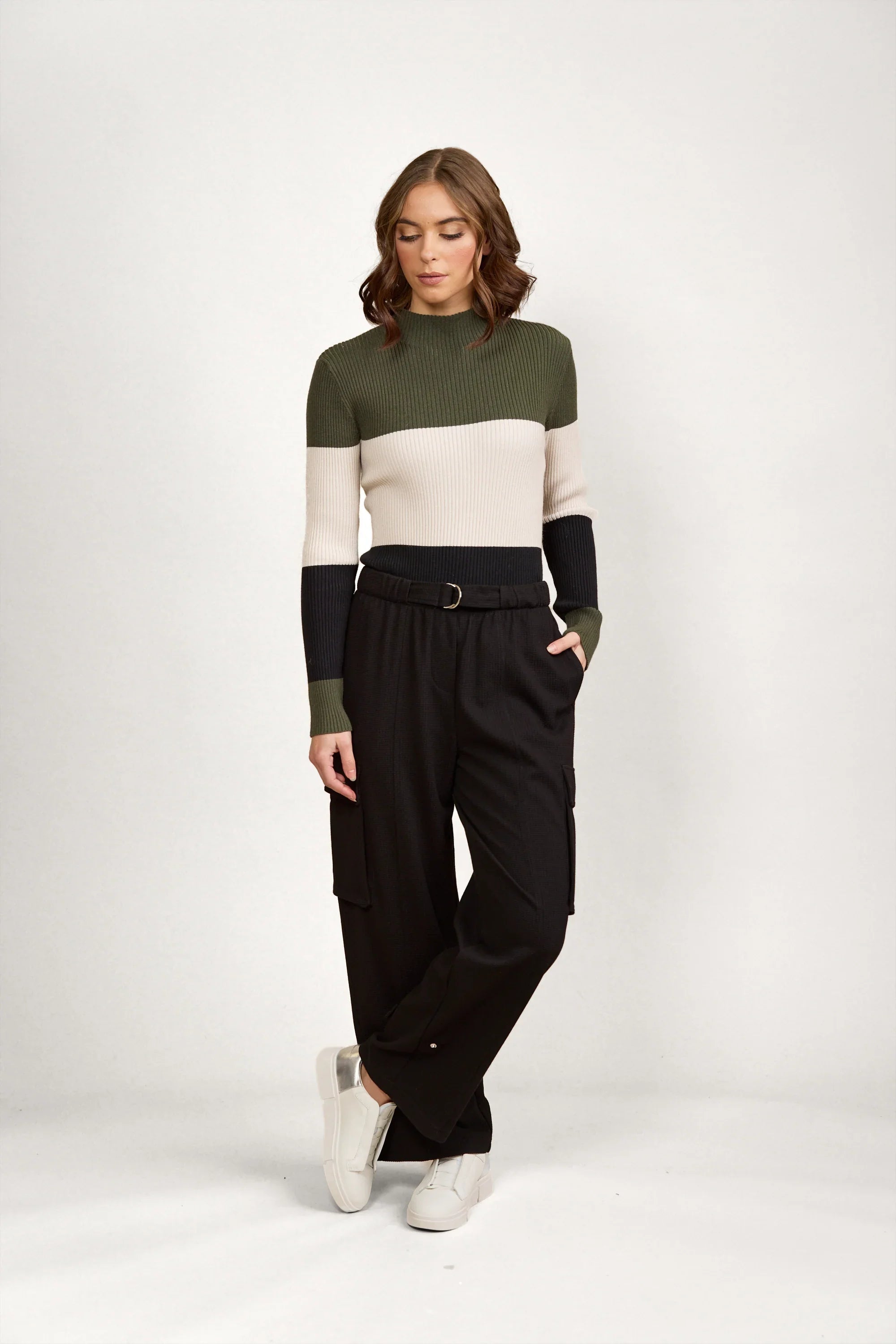 Woman wearing black cargo pants with utility pockets and a colorblock knit top, standing in studio