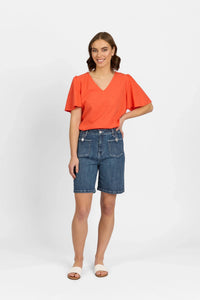 Woman wearing mid-wash denim shorts with front pockets, orange V-neck top, and sandals