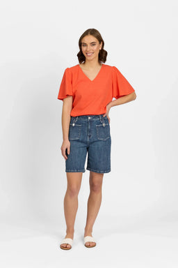 Woman wearing mid-wash denim shorts with front pockets, orange V-neck top, and sandals
