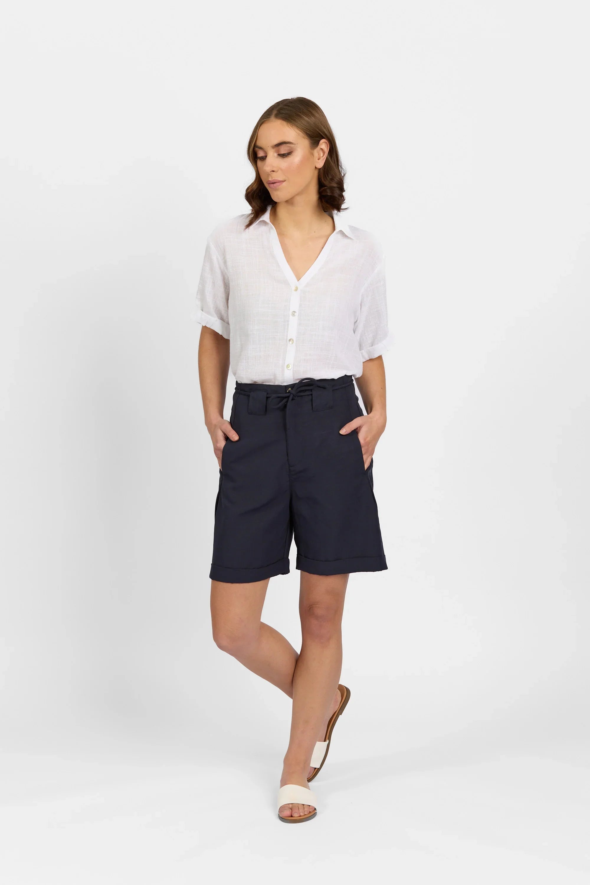 Woman wearing white short-sleeve button-up shirt and navy belted tailored shorts