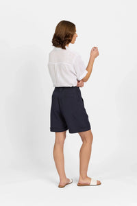 Woman wearing navy tailored shorts and white short-sleeve shirt standing on white background