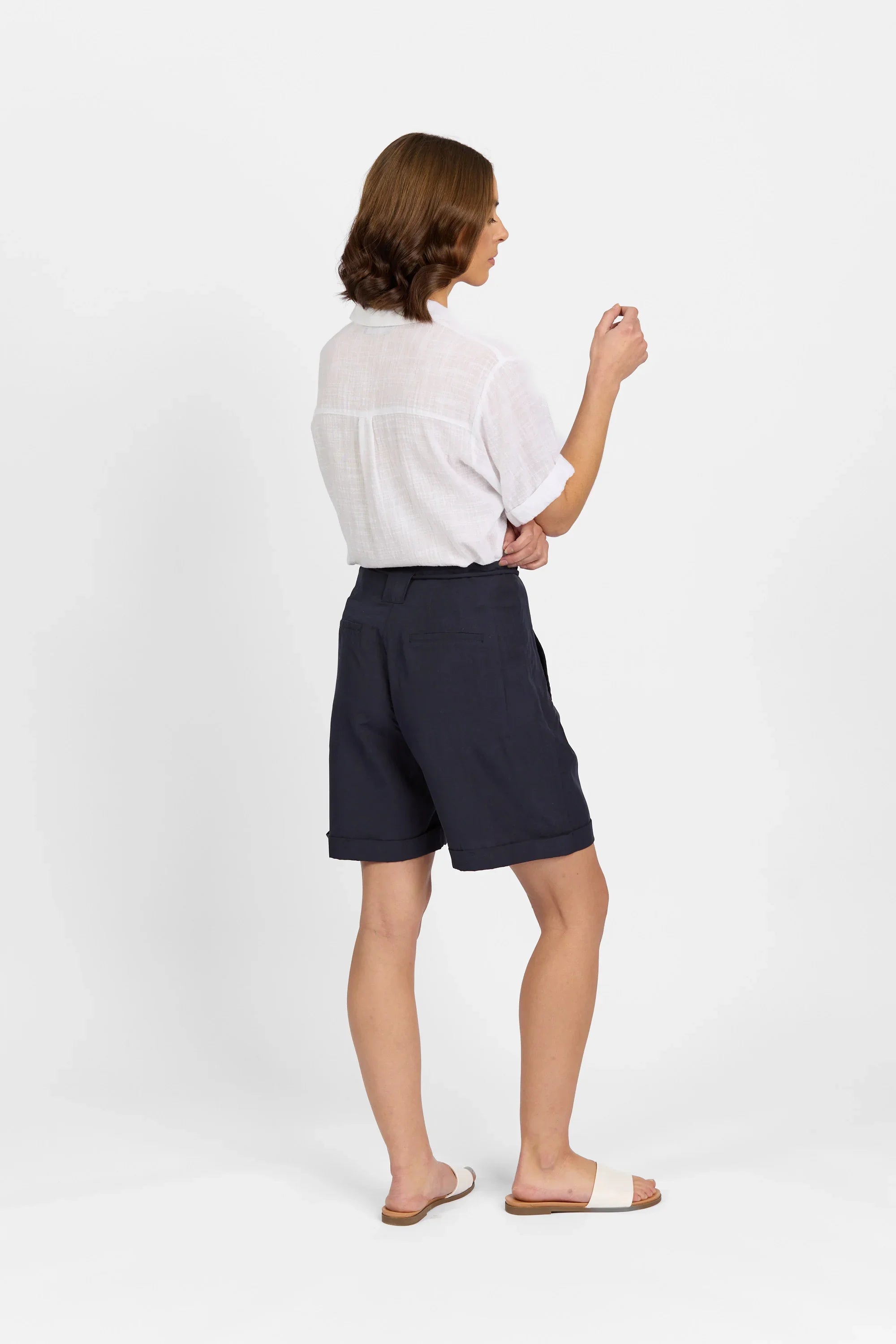Woman wearing navy tailored shorts and white short-sleeve shirt standing on white background