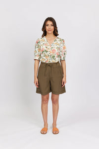 Woman wearing khaki high-waisted shorts and a floral blouse with short sleeves.