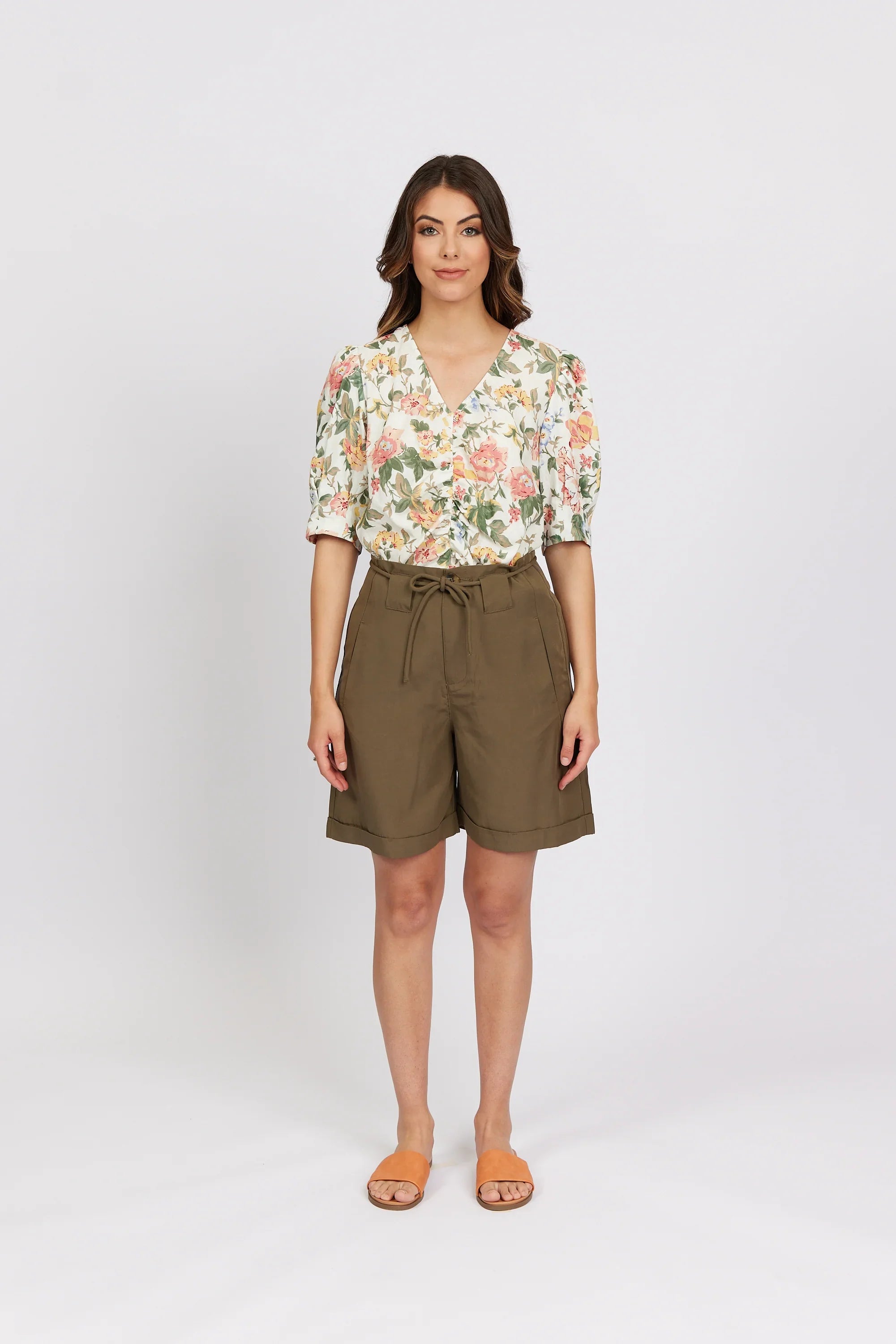 Woman wearing khaki high-waisted shorts and a floral blouse with short sleeves.