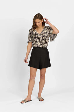 Woman wearing black tailored shorts and patterned short sleeve top, contemporary style
