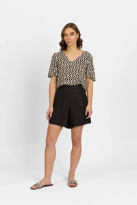 Woman wearing black high-waisted shorts, geometric print top, and slip-on sandals
