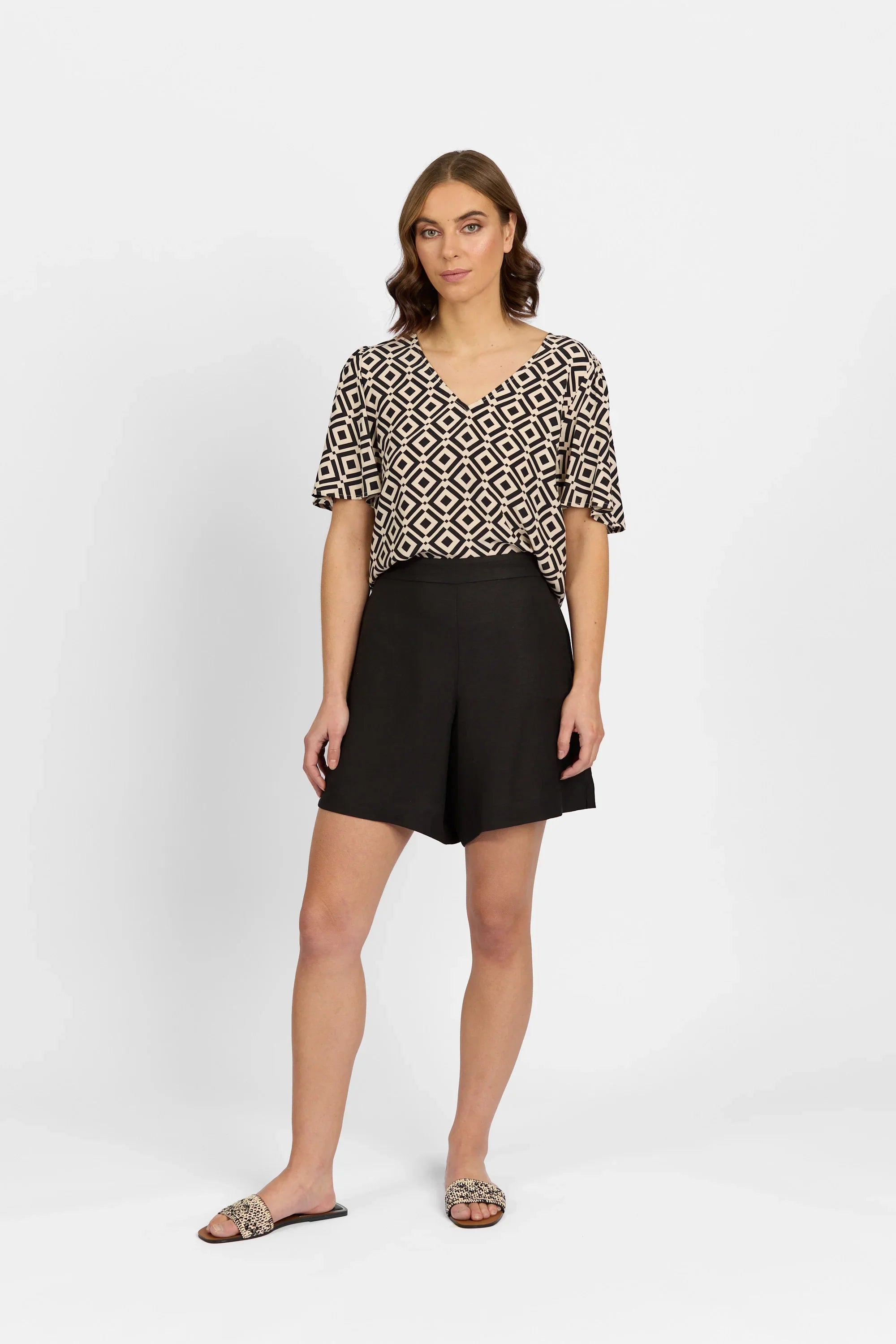 Woman wearing black high-waisted shorts, geometric print top, and slip-on sandals