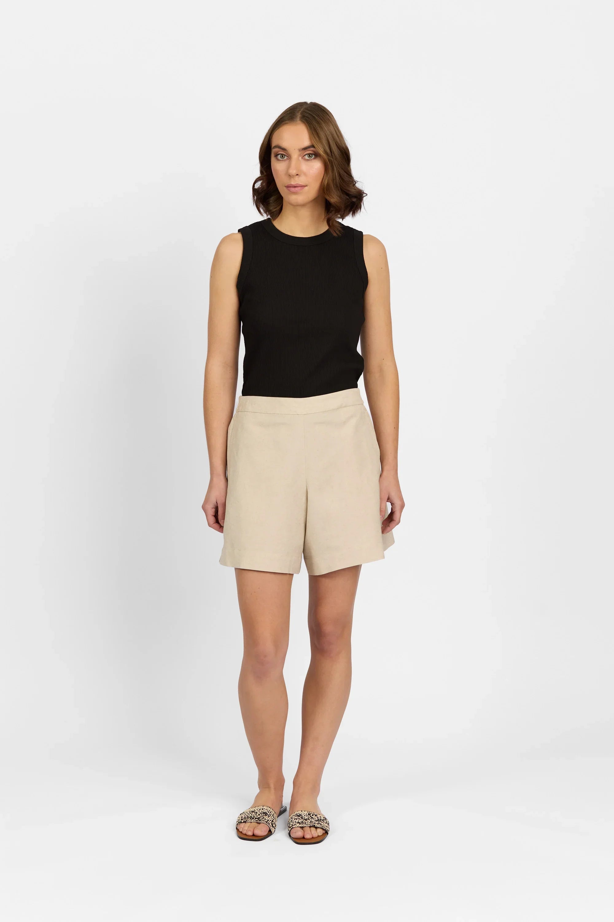 Woman wearing ecru tailored shorts with sleeveless black top and patterned sandals